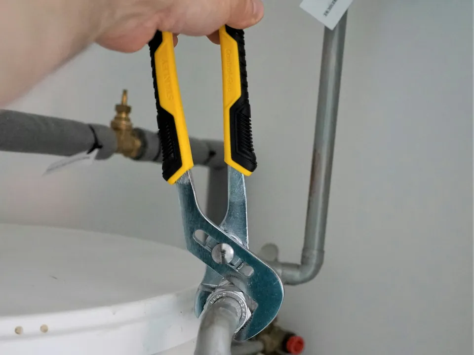 Technicus draait met een waterpomptang een koppeling aan op de leidingen van een warmwaterboiler