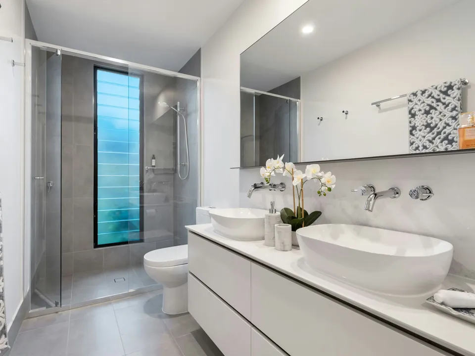 Moderne badkamer met inloopdouche met glazen wand, toilet en een wit badmeubel met twee opzetwaskommen en muurkranen